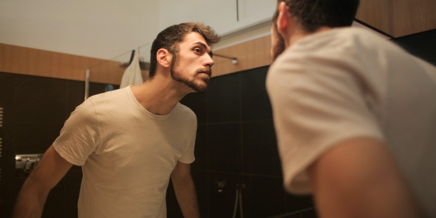 Stylish concentrated man looking in mirror in bathroom