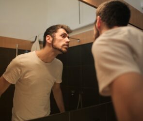 Stylish concentrated man looking in mirror in bathroom