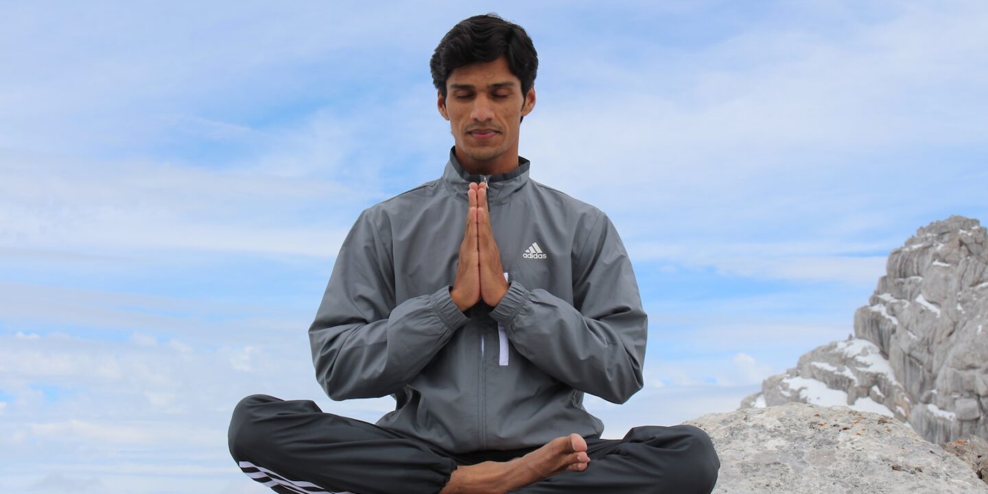 man meditating on brown wooden platform during daytime