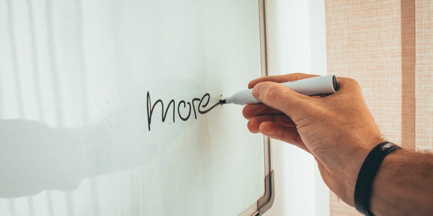 Crop unrecognizable man writing more word with marker on whiteboard during creating new startup in light workplace