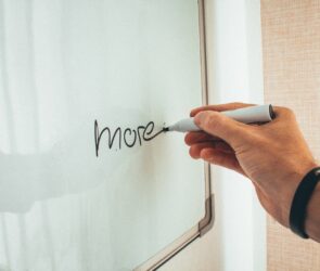 Crop unrecognizable man writing more word with marker on whiteboard during creating new startup in light workplace